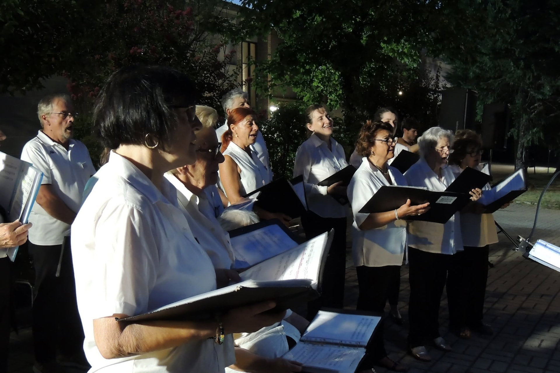Il coro canta di sera all'aperto, con i faldoni delle partiture in mano
