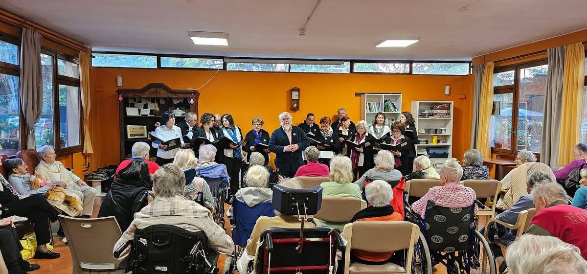 Il coro canta in una sala con le pareti arancioni davanti al pubblico della residenza