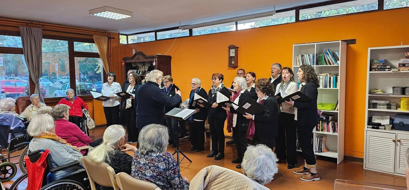 Il maestro dirige il coro nella sala della residenza per anziani, tra libri e poltrone