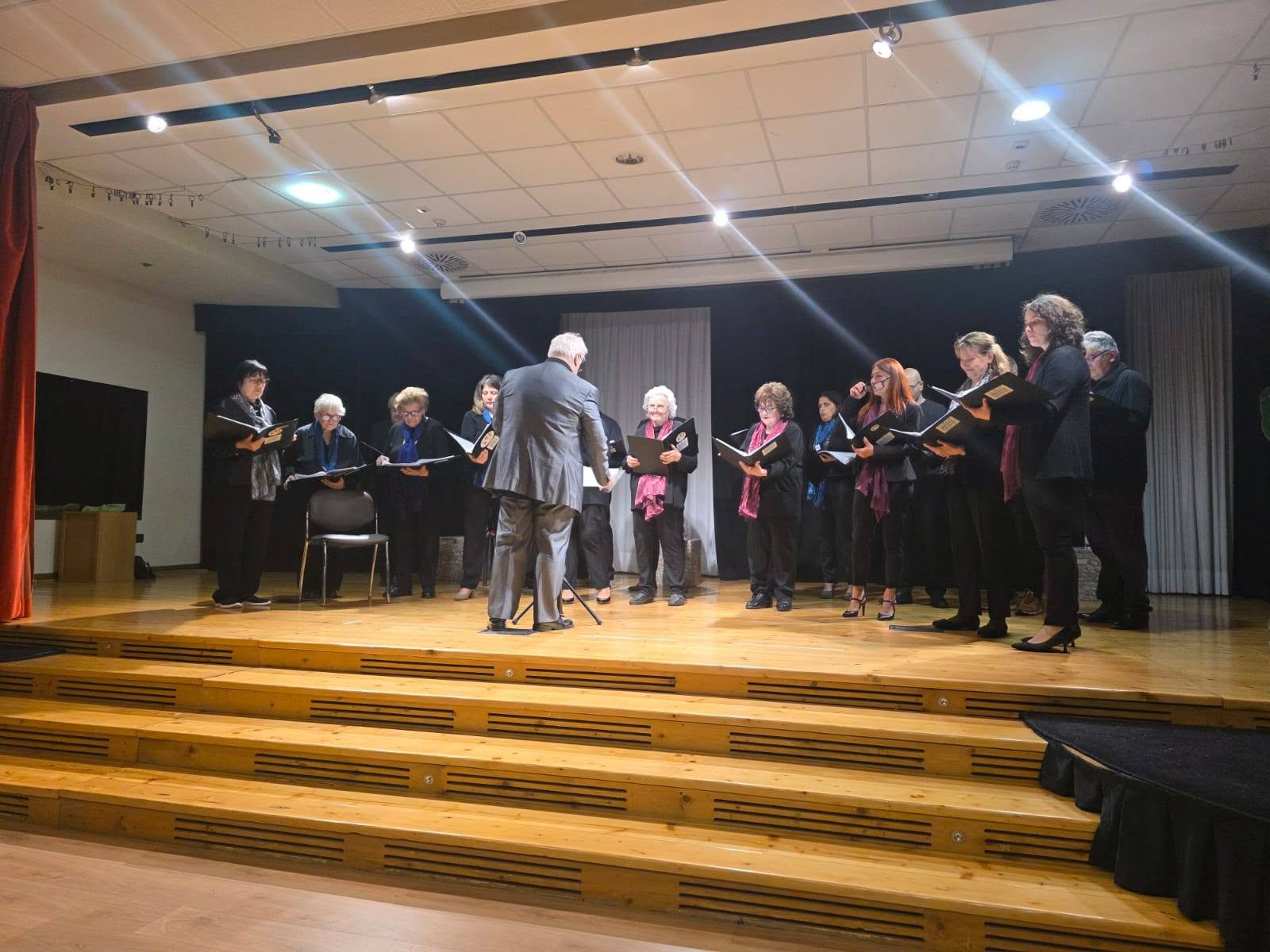 Il coro in concerto sul palco di legno del teatro, sotto le luci della scena